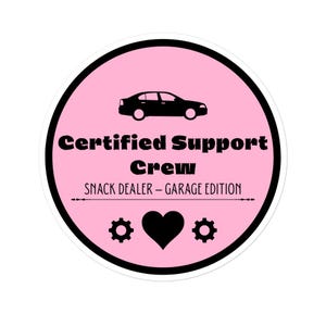 May include: A round sticker with a pink background and a black border. The sticker features a black car silhouette at the top, with the words "Certified Support Crew" in black. Below, it reads "Snack Dealer - Garage Edition". There is a black heart and two gear icons.