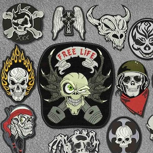 May include: A selection of embroidered patches with skull motifs. The patches depict skulls with flames, wings, and other embellishments. Some patches feature text, including "FREE LIFE". The colour scheme includes black, white, red, and yellow.