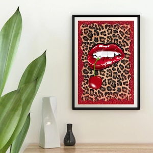 May include: A framed art print featuring a close-up of red lips with white teeth, a cherry, and a leopard print background. The artwork is framed in a black frame and has a red glitter border.