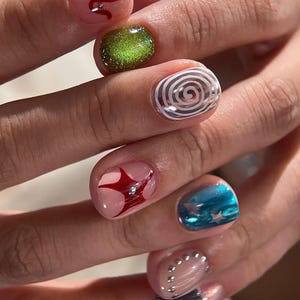 May include: Manicured fingernails featuring diverse nail art designs including a pink base with red swirls and silver studs, a glittery lime green, a white spiral, a red star shape, a blue metallic finish with stars, and silver studs on pink.