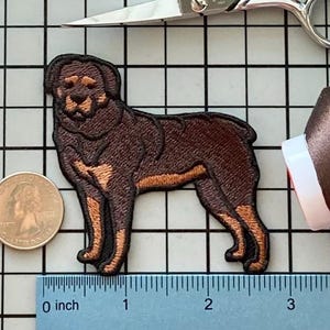 May include: Embroidered patch of a Rottweiler dog in shades of brown and tan. The patch is in a standing position, with detailed stitching. The patch is approximately 3 inches long.