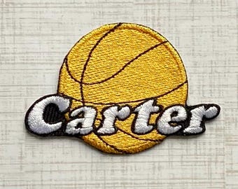 Könnte beinhalten: Ein kreisförmiger gestickter Aufnäher mit einem gelben Basketball mit schwarzen Linien. Der Name Carter ist in der Mitte mit weißem Garn und schwarzer Umrandung aufgestickt, was einen Schichteffekt über dem Basketball-Grafikdesign erzeugt.