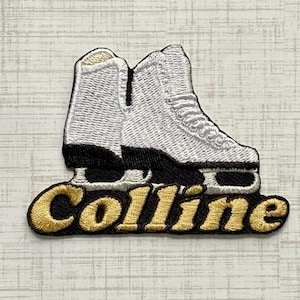 Peut inclure: Un écusson brodé représentant une paire de patins à glace blancs avec des lames et des semelles noires. Sous les patins, le mot Colline est brodé en fil doré avec un contour noir. Le motif est réalisé dans un style de broderie dense et texturé.