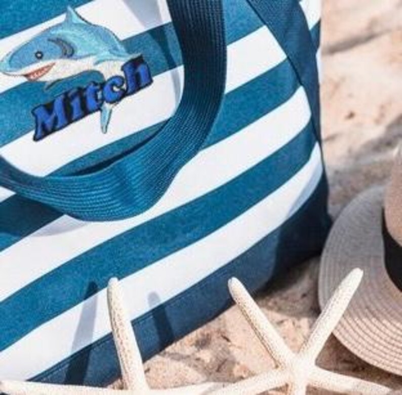 May include: Blue and white striped canvas tote bag with a blue shark and the name Mitch embroidered on it.