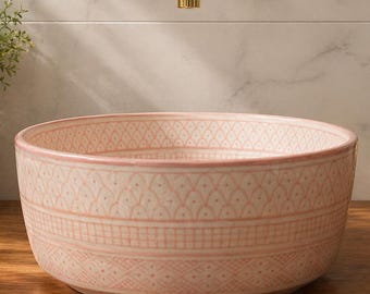 May include: A pink and white patterned ceramic sink bowl. The sink is on a wooden surface, with gold taps and a mirror in the background. A gold pineapple-shaped soap dispenser is to the right. The sink is a decorative bathroom fixture.