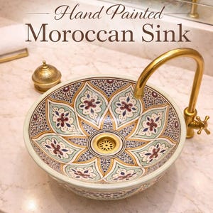 May include: Hand-painted Moroccan sink with a floral design in shades of blue, green, and red. The sink has a gold-colored faucet and drain. The text "Hand Painted Moroccan Sink" is displayed above the sink.