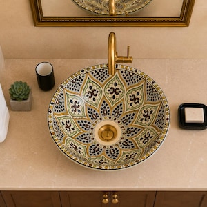 May include: A round ceramic vessel sink featuring a detailed floral and geometric pattern in shades of green, brown, and black. The sink is mounted on a light beige countertop with a gold-toned faucet, a black soap dish, and a small succulent.