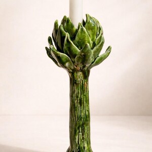 Può includere: Un portacandele a forma di carciofo in ceramica verde con una candela bianca. Il portacandele ha uno stelo strutturato e foglie dettagliate. Un elemento decorativo unico per la casa.