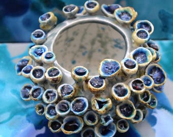 Puede incluir: Un jarrón de cerámica con un diseño único en forma de coral. El jarrón presenta una base azul claro con numerosas protuberancias pequeñas y redondeadas en tonos de azul, amarillo y negro. El interior del jarrón es visible, mostrando un patrón moteado.
