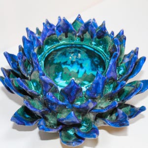 Può includere: Una ciotola in ceramica a forma di fiore di loto con una tavolozza di colori vivaci. La ciotola presenta un esterno blu scuro e verde acqua con finitura lucida. L'interno è di una tonalità verde acqua più chiara. I petali sono dettagliati e strutturati.
