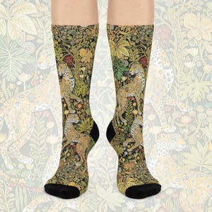 May include: A pair of socks featuring a detailed jungle scene with leopards and lush foliage in shades of green, yellow, and red. The socks have black heels and toes, and the design is repeated on a light background.