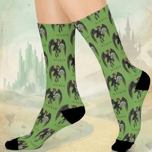 May include: Green socks with a repeating pattern of a winged character holding a crystal ball, with the word "WICKED" printed above the character. The socks have black heels and toes.