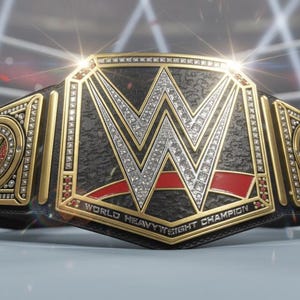 May include: A close-up of a WWE World Heavyweight Championship belt. The belt is black with gold accents, a large silver "W" logo, and red detailing. The words "World Heavyweight Champion" are visible. The background is a wrestling ring.