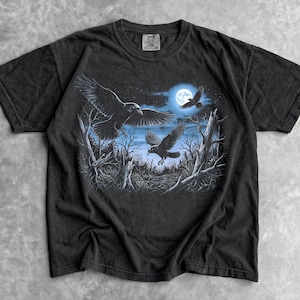 May include: Black t-shirt featuring a graphic of three eagles soaring in a moonlit forest. The design includes a full moon and bare trees, creating a nocturnal scene. The word "Black" is printed at the bottom.