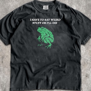 May include: A black short-sleeve t-shirt featuring a green graphic of a frog centered on the chest. Above the frog, the white text reads, I HAVE TO SAY WEIRD STUFF OR I'LL DIE. The shirt has a crew neckline and a standard fit with a visible brand tag.