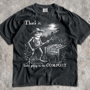May include: Black t-shirt with a humorous graphic of a frog in overalls holding a pitchfork, standing near a compost bin. The text reads "That's it. You're going in the COMPOST."