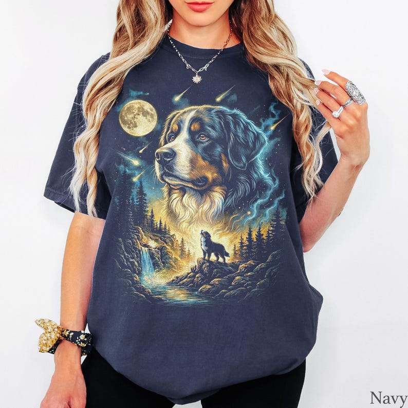 May include: A navy blue short-sleeve t-shirt featuring a graphic print of a Bernese Mountain Dog head above a smaller silhouette of a dog standing on a rocky cliff near a waterfall, set against a night sky with a full moon and falling stars.