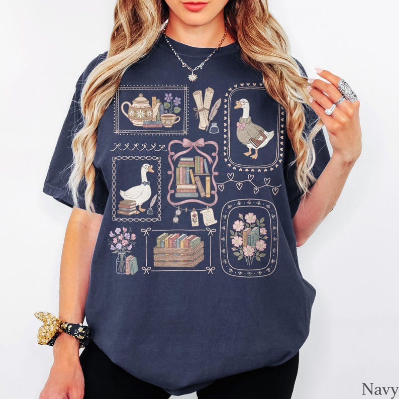 Puede incluir: Una camiseta azul marino con un estampado gr&aacute;fico de varias ilustraciones enmarcadas que incluyen gansos con gafas, pilas de libros, una tetera, una taza de t&eacute;, flores y pergaminos. El dise&ntilde;o est&aacute; dispuesto en un patr&oacute;n de cuadr&iacute;cula.