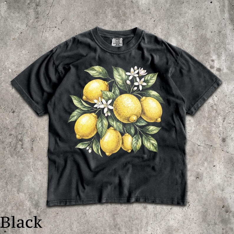 Może przedstawiać: Czarny t-shirt z akwarelową ilustracją cytryn, liści i białych kwiat&oacute;w. Projekt przedstawia ż&oacute;łte cytryny z zielonymi liśćmi i białymi kwiatami, tworząc letni, botaniczny motyw.