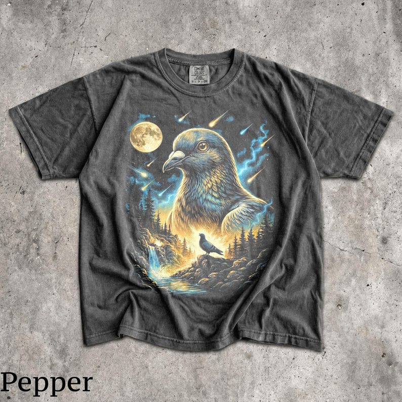 May include: A charcoal grey short-sleeve t-shirt featuring a graphic print of a large pigeon head against a night sky with a full moon, falling stars, and blue lightning. Below, a smaller pigeon stands on a rocky cliff near a waterfall and forest.