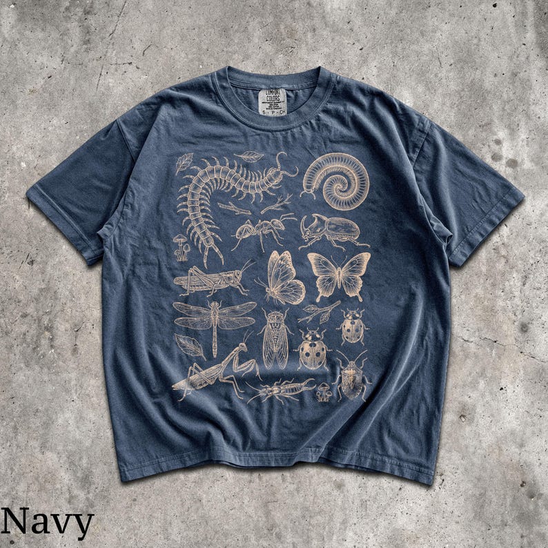 May include: A navy blue short-sleeve t-shirt featuring a detailed, light-colored graphic print of various insects, including a centipede, butterfly, dragonfly, beetle, and mantis, arranged across the front with a visible neck label.