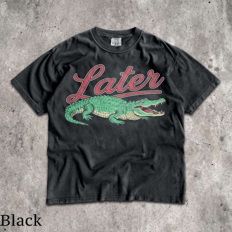 Puede incluir: Camiseta negra con un dise&ntilde;o de cocodrilo verde y la palabra "Later" en letras rojas. El cocodrilo tiene la boca abierta. La camiseta es de cuello redondo y est&aacute; hecha de un material suave.