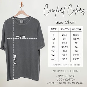 May include: A charcoal gray short-sleeve t-shirt hanging on a wooden hanger, accompanied by a Comfort Colors size chart. The chart lists sizes S through 4XL with corresponding length and width measurements in inches for the 1717 unisex tee shirt.