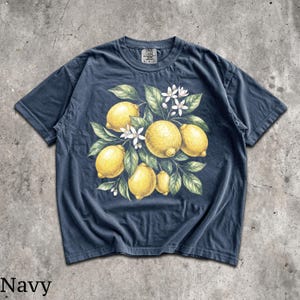 Może przedstawiać: Granatowa koszulka z akwarelową ilustracją cytryn, liści i białych kwiat&oacute;w. Projekt jest wyśrodkowany z przodu. Słowo "Navy" jest wydrukowane w lewym dolnym rogu.