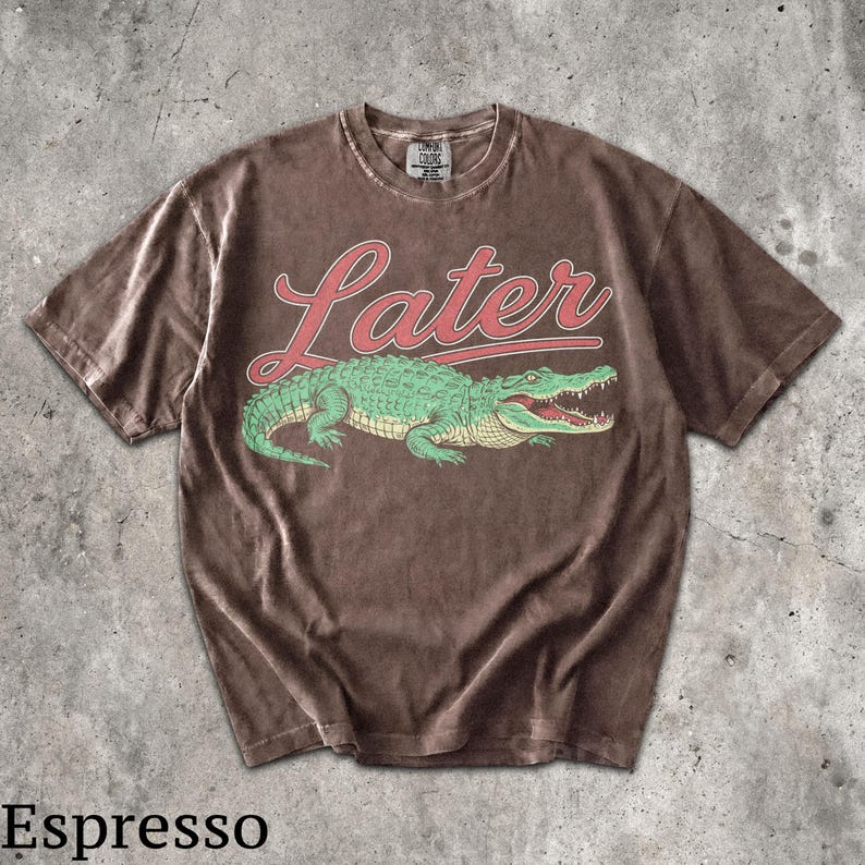 Puede incluir: Camiseta color espresso con un gr&aacute;fico de un cocodrilo verde y la palabra "Later" en escritura roja. La camiseta tiene un aspecto vintage y desgastado, con cuello redondo. La etiqueta de la marca es visible en la parte superior.