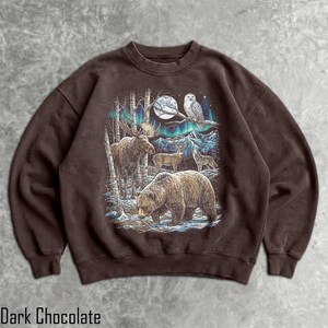 Pu&ograve; includere: Felpa color cioccolato fondente con una scena di foresta con un orso, un alce, cervi e un lupo sotto l'aurora boreale. Un gufo &egrave; appollaiato su un ramo vicino alla luna piena. Il testo "Dark Chocolate" &egrave; in basso.