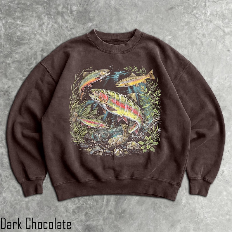 May include: A dark chocolate brown crewneck sweatshirt featuring a detailed graphic print of three rainbow trout swimming among green aquatic plants and rocks. The illustration displays the fish with vibrant scales and distinct markings.