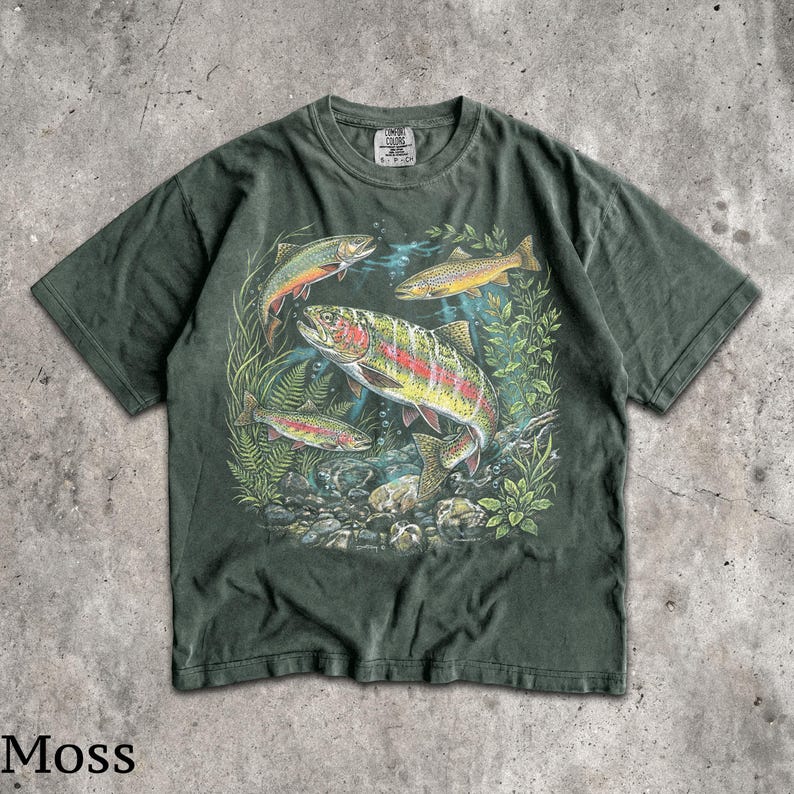 May include: Moss green t-shirt featuring a colorful graphic of several trout swimming amongst aquatic plants and rocks. The fish have vibrant red, yellow, and orange markings. The shirt has a classic crew neck and short sleeves.