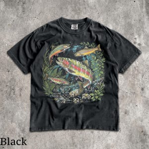 May include: Black t-shirt featuring a colorful illustration of several trout swimming in a freshwater environment. The design includes various fish species, aquatic plants, and rocks, creating a detailed and vibrant scene. The shirt's color is black.
