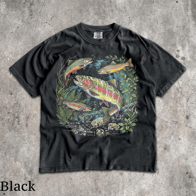 May include: Black t-shirt featuring a colorful illustration of several trout swimming in a freshwater environment. The design includes various fish species, aquatic plants, and rocks, creating a detailed and vibrant scene. The shirt's color is black.