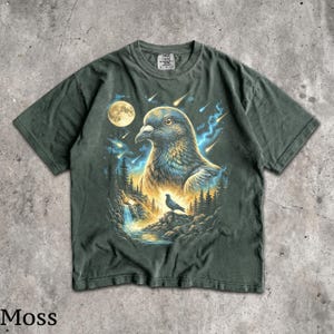 May include: A dark green t-shirt featuring a graphic print of a large pigeon head in the sky above a smaller pigeon perched on a rocky cliff near a waterfall. The scene includes a full moon, glowing blue energy streaks, and falling stars.