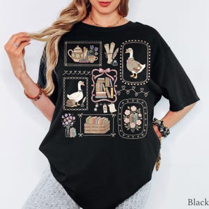 Puede incluir: Una camiseta negra de manga corta con un estampado gr&aacute;fico de varias ilustraciones enmarcadas que incluyen gansos, pilas de libros, una tetera, flores y plumas de escribir, dispuestas en un estilo de collage con bordes decorativos.