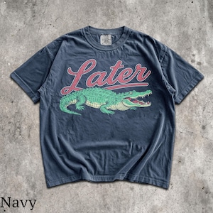 Puede incluir: Camiseta azul marino con un gr&aacute;fico de un cocodrilo verde y la palabra "Later" en escritura roja. La camiseta tiene cuello redondo y mangas cortas. La palabra "Navy" est&aacute; impresa en la parte inferior de la imagen.