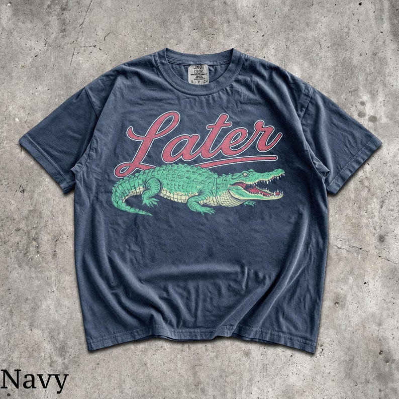 Puede incluir: Camiseta azul marino con un gr&aacute;fico de un cocodrilo verde y la palabra "Later" en escritura roja. La camiseta tiene cuello redondo y mangas cortas. La palabra "Navy" est&aacute; impresa en la parte inferior de la imagen.