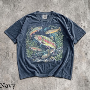May include: Navy blue t-shirt featuring a colorful illustration of several trout swimming amongst aquatic plants and rocks. The graphic includes fish with red, yellow, and silver scales. The word "Navy" is printed at the bottom of the shirt.