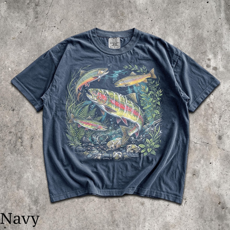 May include: Navy blue t-shirt featuring a colorful illustration of several trout swimming amongst aquatic plants and rocks. The graphic includes fish with red, yellow, and silver scales. The word "Navy" is printed at the bottom of the shirt.