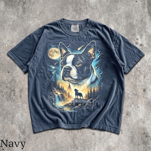 K&ouml;nnte beinhalten: Ein marineblaues Kurzarm-T-Shirt mit einem Grafikdruck eines Boston Terrier-Gesichts, einem Vollmond, der Silhouette eines heulenden Hundes in einer Waldlandschaft mit Wasserfall und Sternschnuppen vor einem blau-gelb leuchtenden Hintergrund.