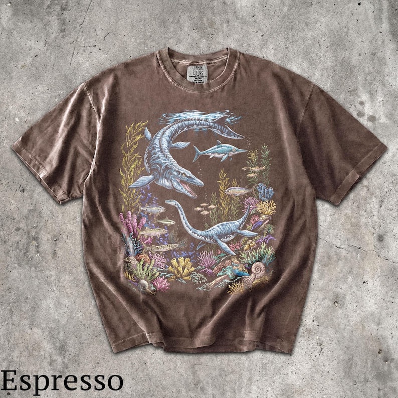 Op de afbeelding: Espresso-kleurig T-shirt met een gedetailleerde illustratie van prehistorisch zeeleven, waaronder plesiosauri&euml;rs en vissen, tegen een kleurrijke koraalrif achtergrond. Het shirt heeft een vintage, gewassen look.