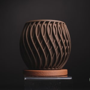 May include: A brown, decorative vase with a unique, woven design. The vase sits on a small, round, brown base. The vase is made of a solid material and has a textured surface. The overall shape is oval.