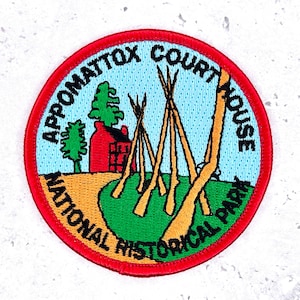 May include: Embroidered patch with a red border featuring the text "Appomattox Court House National Historical Park." The patch depicts a red building, teepees, and trees on a green and yellow landscape against a blue sky.