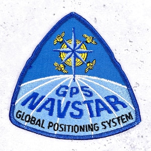 May include: A blue embroidered patch with a white and blue globe design, a blue star, and the words "GPS NAVSTAR GLOBAL POSITIONING SYSTEM." The patch also features four yellow satellite illustrations.