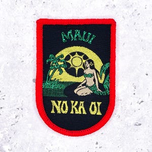 Op de afbeelding: Zwarte patch met een rode rand met een tropische scène. Het ontwerp bevat een gele zon, palmbomen en een zeemeermin. De teksten "MAUI" en "NO KA OI" zijn respectievelijk groen en geel.
