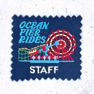 May include: A navy blue embroidered patch with the words "OCEAN PIER RIDES STAFF". The patch features a Ferris wheel, roller coaster, and other amusement park ride designs in red, yellow, and blue.