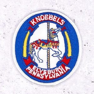 May include: Embroidered patch with a carousel horse design. The patch features the text "Knoebels" in red on a blue banner at the top and "Elysburg Pennsylvania" in white at the bottom. The carousel horse is white with red and yellow accents.