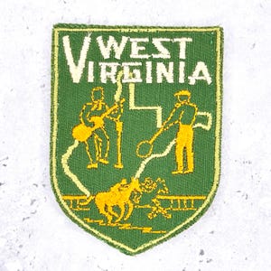 May include: A shield-shaped embroidered patch in green with a yellow border. The text WEST VIRGINIA is stitched in white at the top. Below, yellow thread depicts a person playing a guitar, a person holding a hoop, and a horse with a rider.