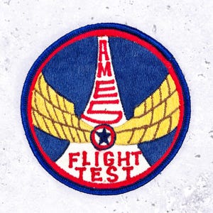 Puede incluir: Una taza de cerámica blanca con asa negra y el texto "But First, Coffee" en negrita negra. La taza se encuentra sobre un fondo borroso, sugiriendo un ambiente acogedor.